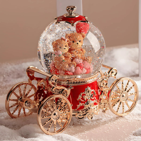 Decorative snow globe with teddy bears and a red carriage base on a white surface.