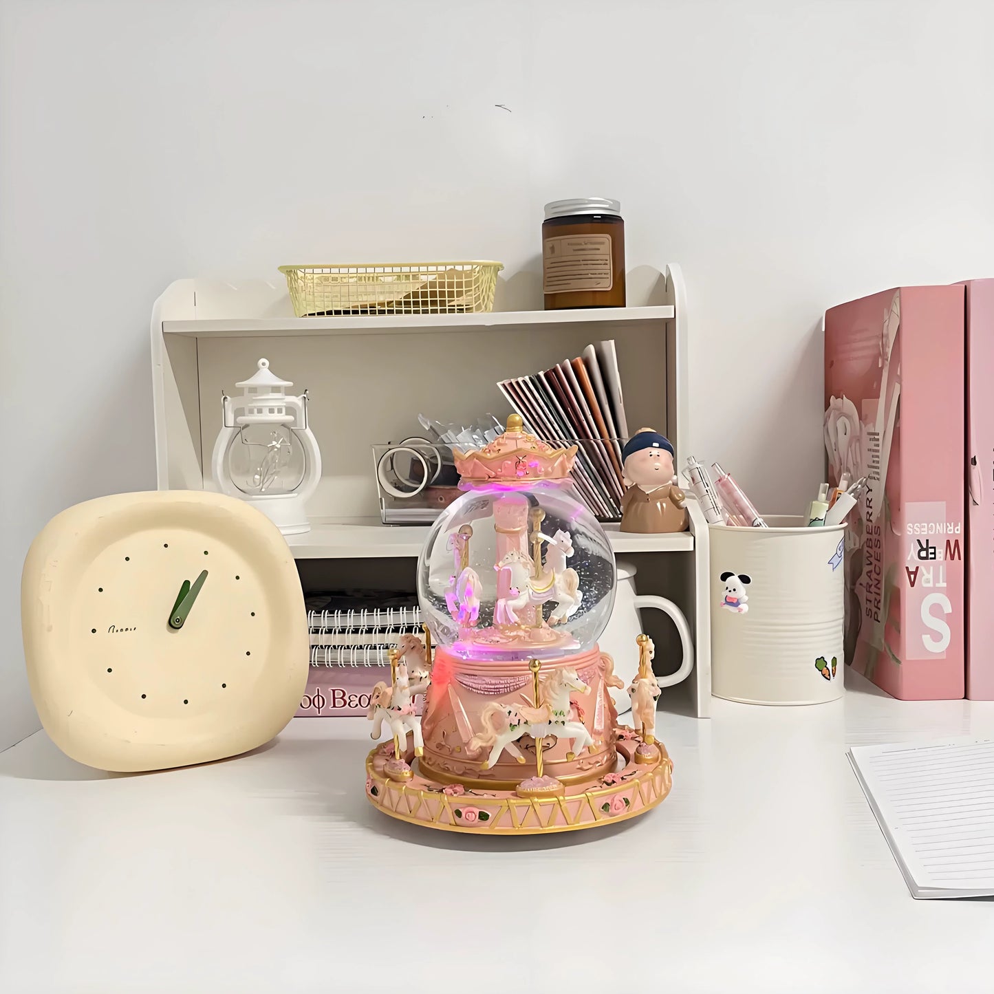 Decorative snow globe with carousel design on a desk with a clock and books in the background.