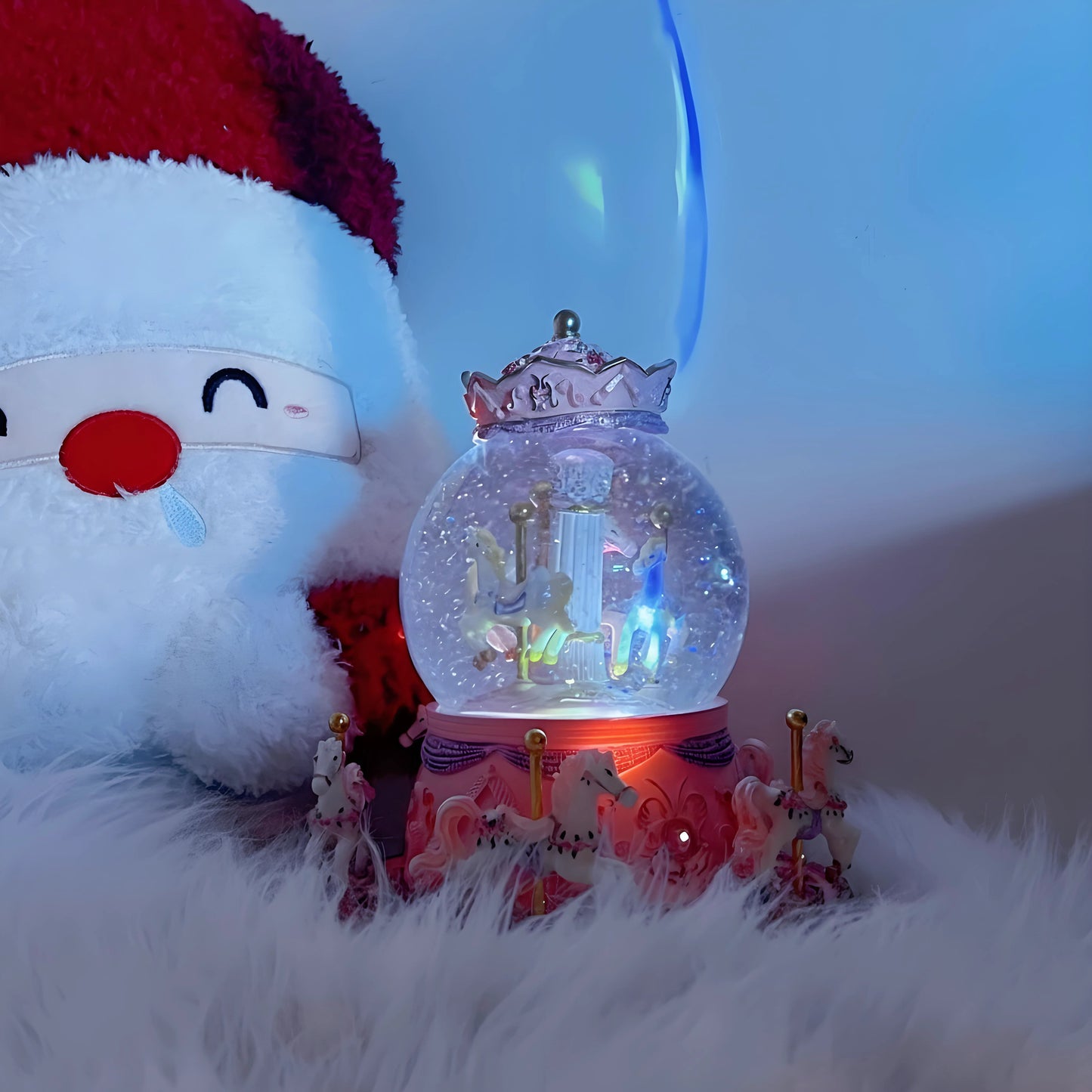Snow globe with unicorn design on a fluffy surface next to a plush toy with a red hat.