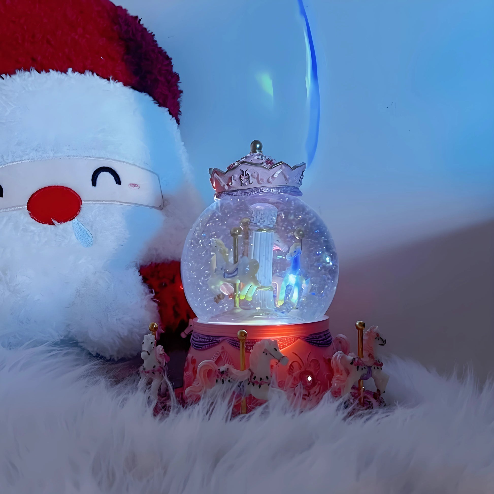 Snow globe with unicorn design on a fluffy surface next to a plush toy with a red hat.