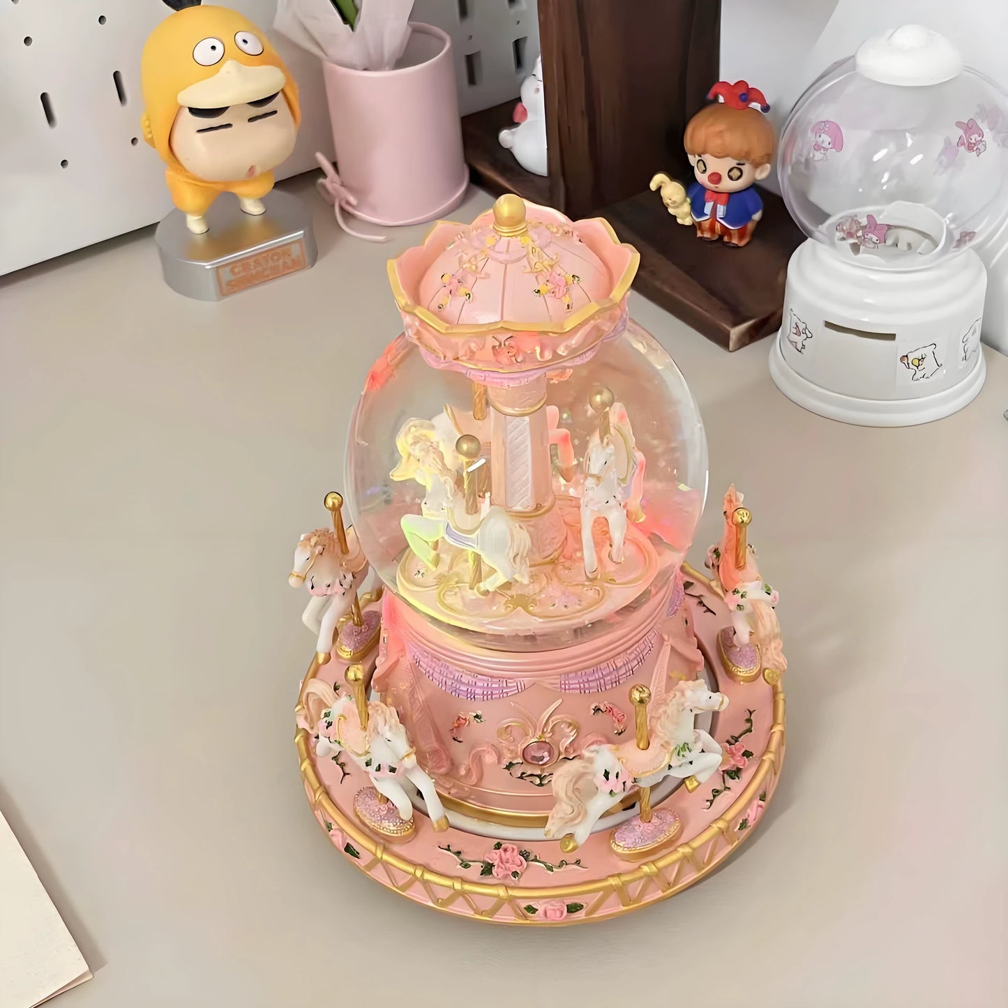 Decorative pink carousel with moving figures inside a glass dome on a white surface.