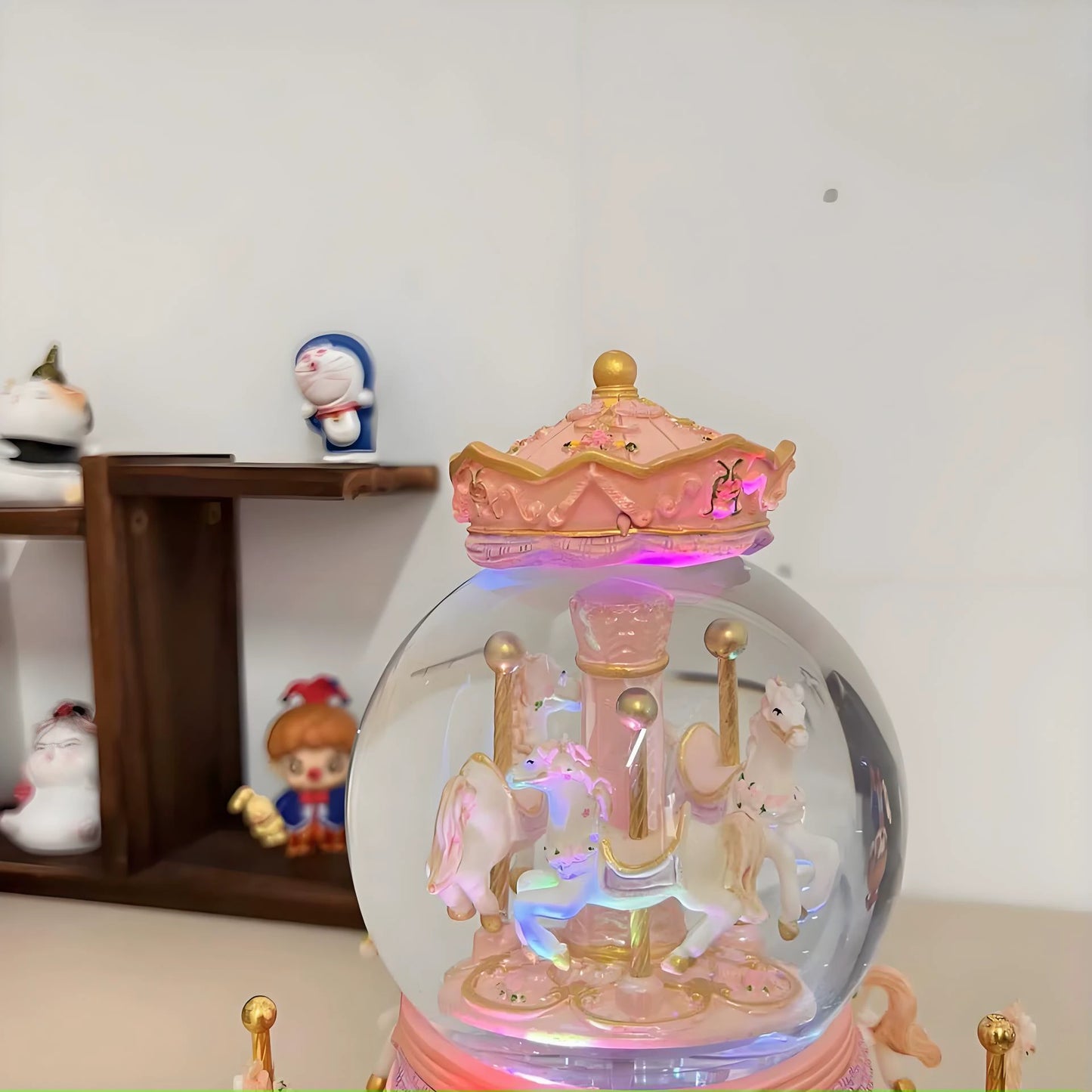 Decorative snow globe with carousel horses and colorful lights on a shelf.