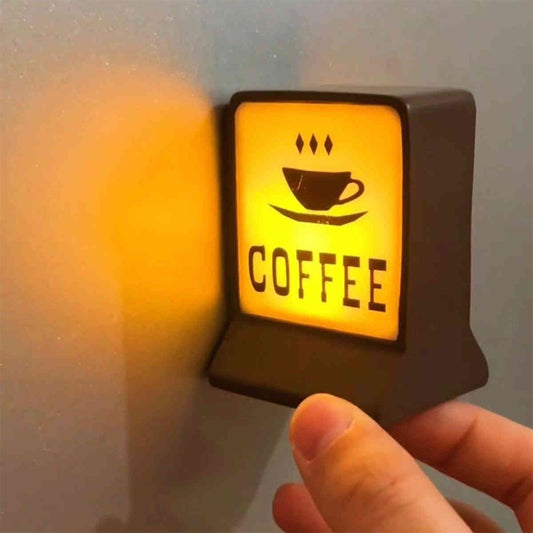 A rectangular LED sign with a coffee cup icon and the word 'COFFEE' illuminated in capital letters. The sign is mounted on a wall with a hand reaching for it.