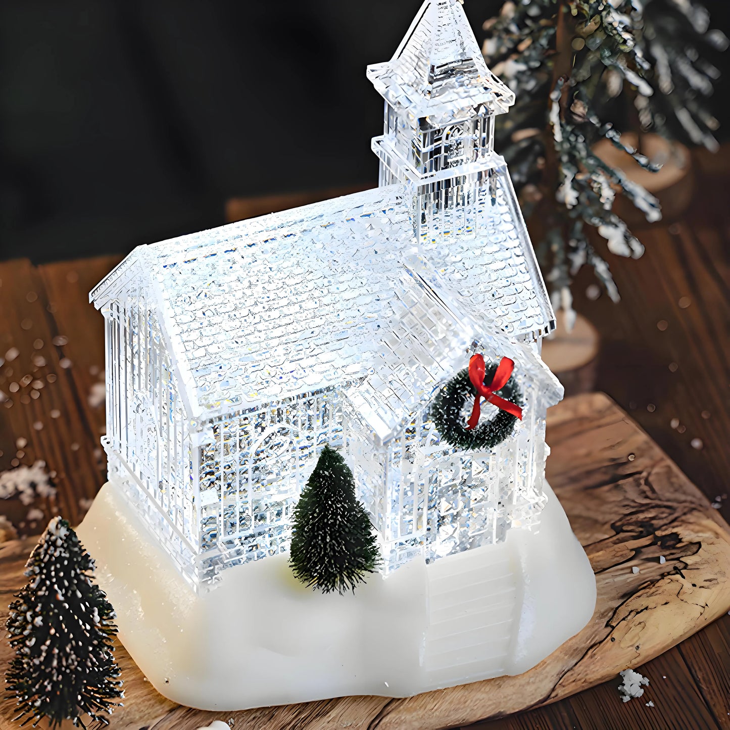 Illuminated glass church model with a wreath on a wooden surface