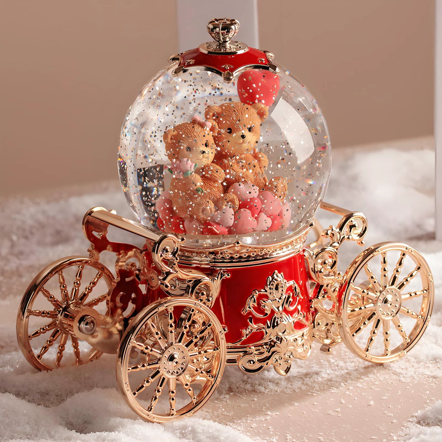 Decorative snow globe with teddy bears and a red carriage base on a white surface.