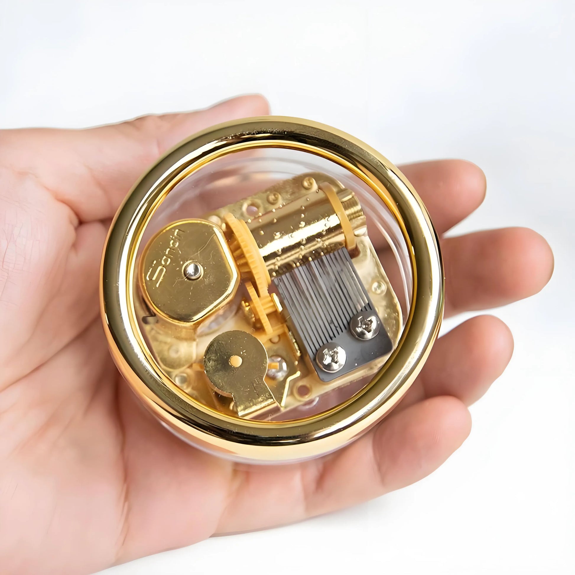 Compact vintage style wind-up music box, transparent body, visible golden clockwork mechanism